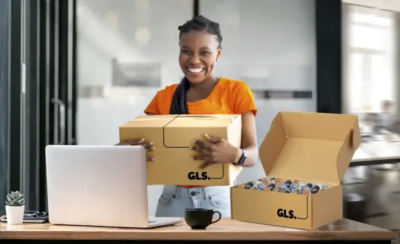 A smiling woman holding a GLS parcel in an office setting.