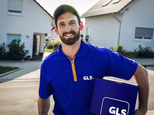 GLS courier stands with parcel in front of house