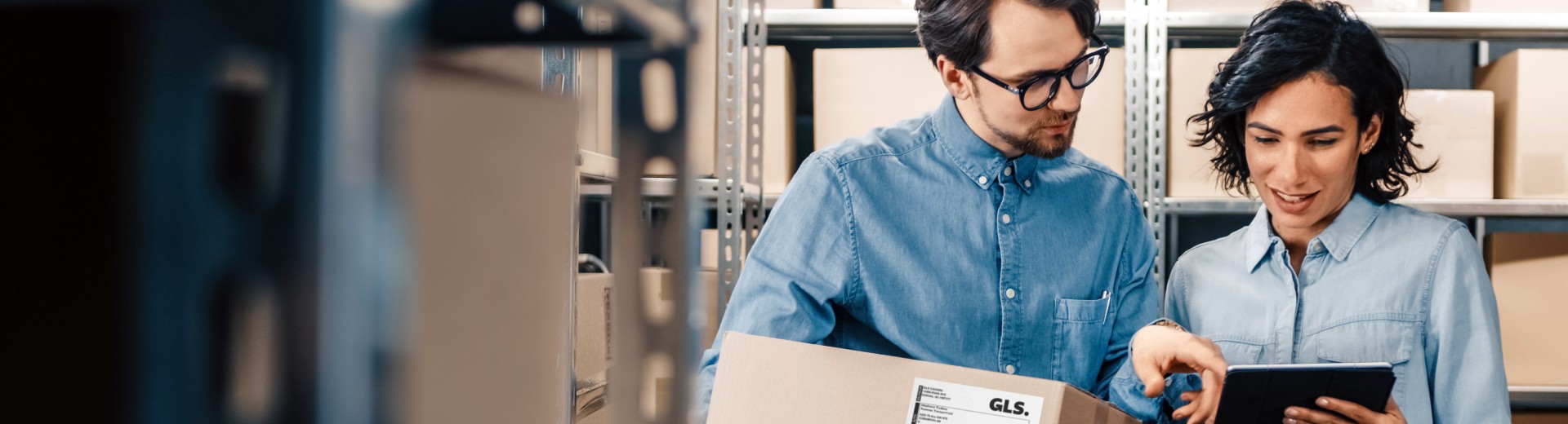 Two people in a warehouse with a box looking at a tablet