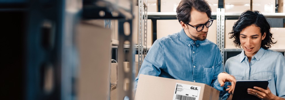 Two people in a warehouse with a box looking at a tablet