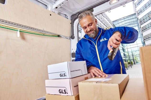 A GLS driver scans a parcel in the back of a delivery van.